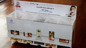 Opal acrylic gravity fed dispensing unit housing coffee sachets with a coin donation section.