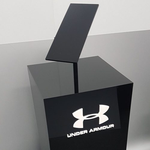 Custom black acrylic plinth with angled display set on top. White acrylic logo adhered to the front face.