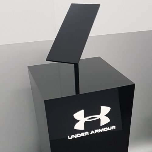 Custom black acrylic plinth with angled display set on top. White acrylic logo adhered to the front face.