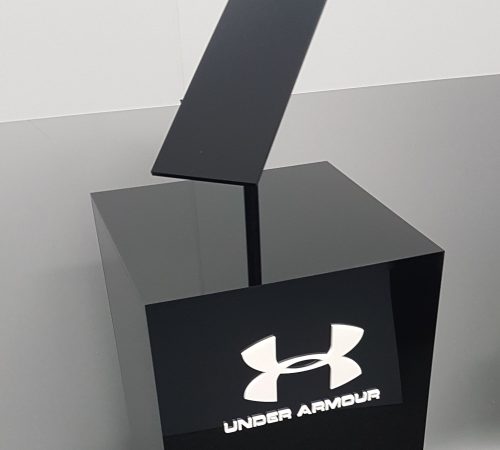 Custom black acrylic plinth with angled display set on top. White acrylic logo adhered to the front face.