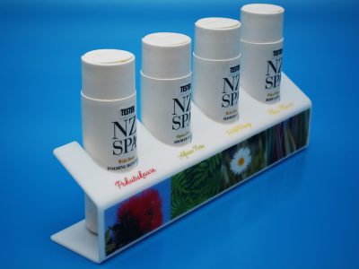 White acrylic display stand, bent and printed, housing spa products in sectioned cut-outs.